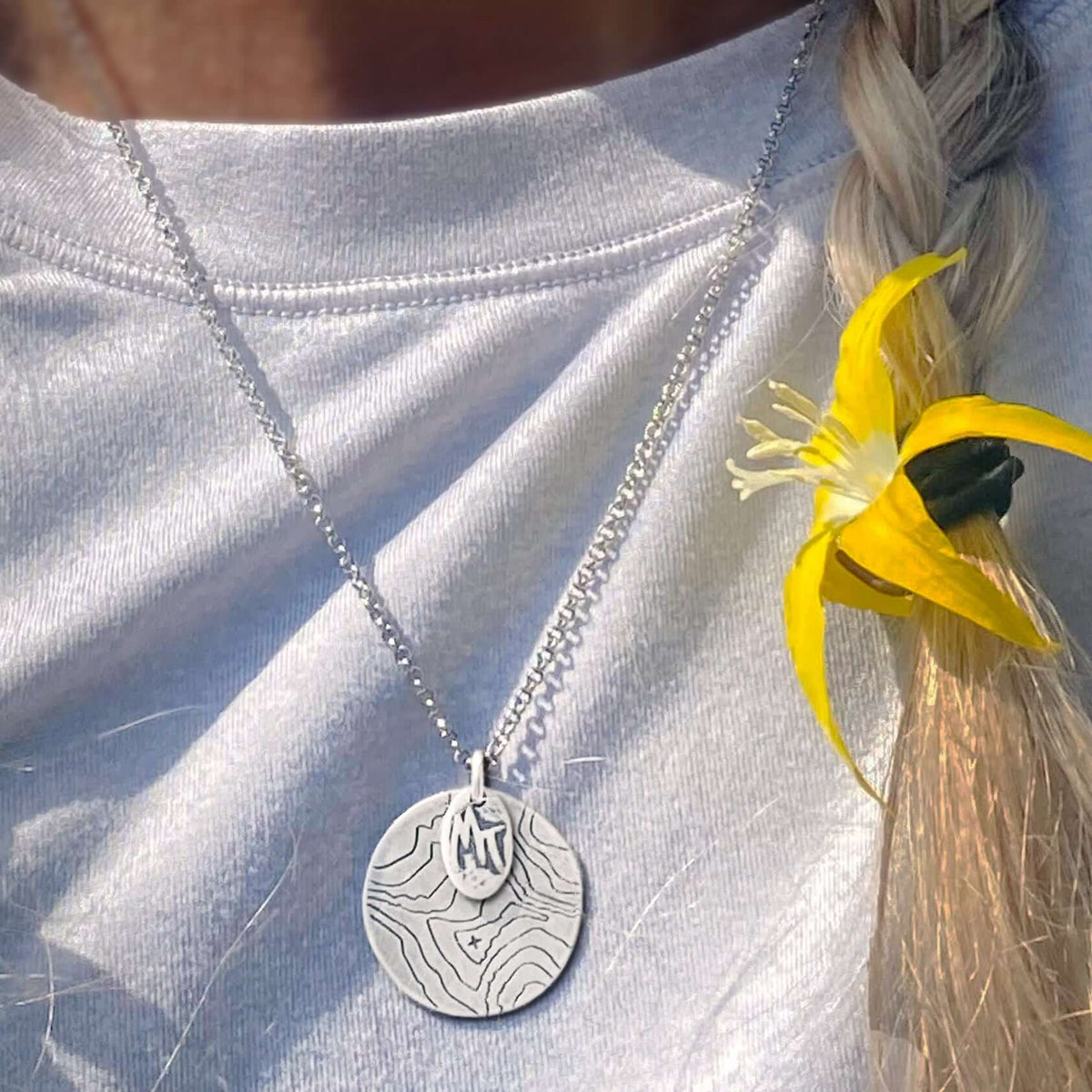 Explore MT Necklace showcasing topographic map design in matte silver, resting on a model's neckline.