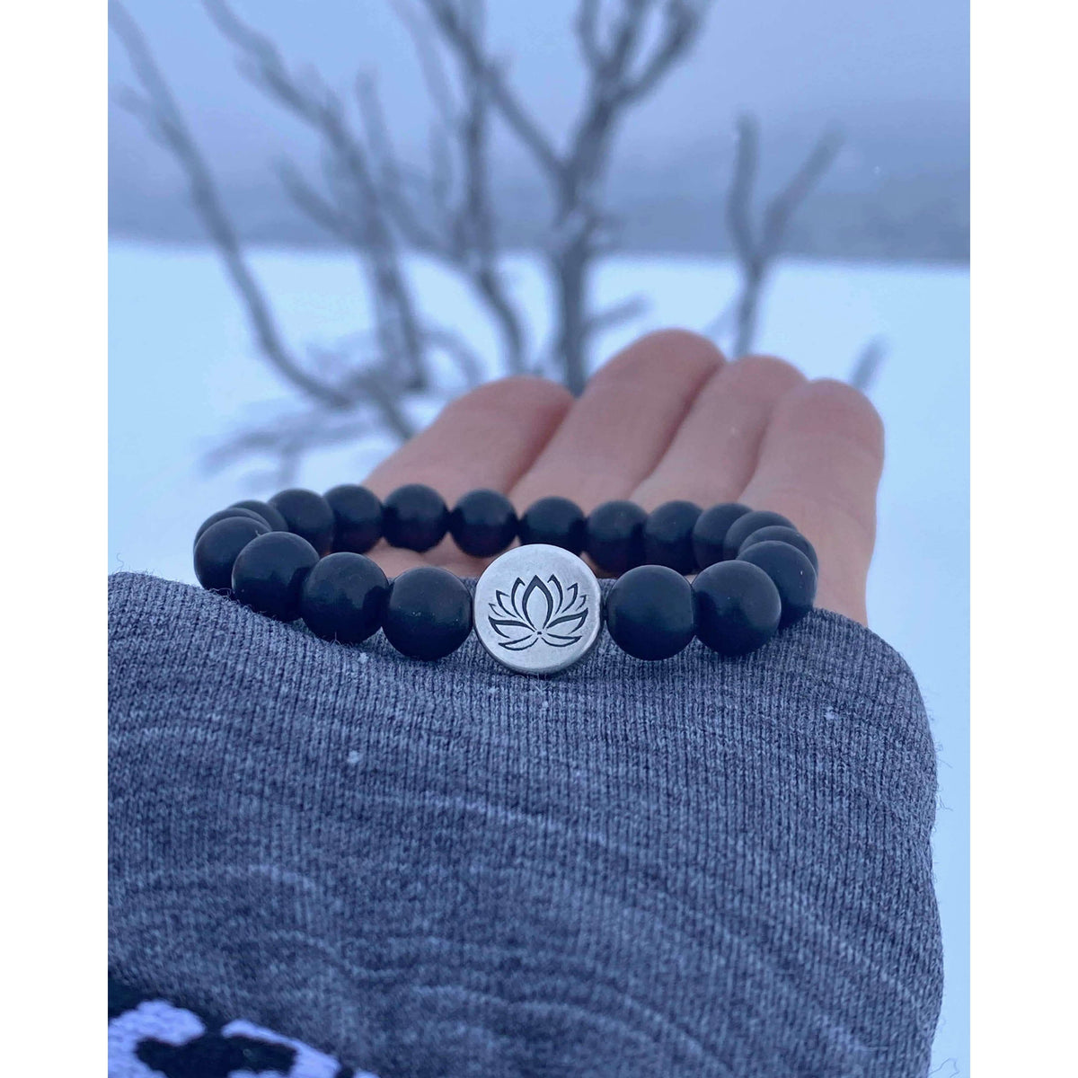 Lotus Stretch Bracelet - Gemstone Beaded Stretchy Bracelet with black beads and silver lotus charm in a snowy landscape.