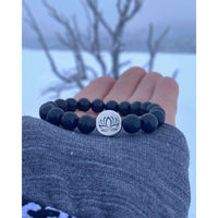 Lotus Stretch Bracelet - Gemstone Beaded Stretchy Bracelet with black beads and silver lotus charm in a snowy landscape.