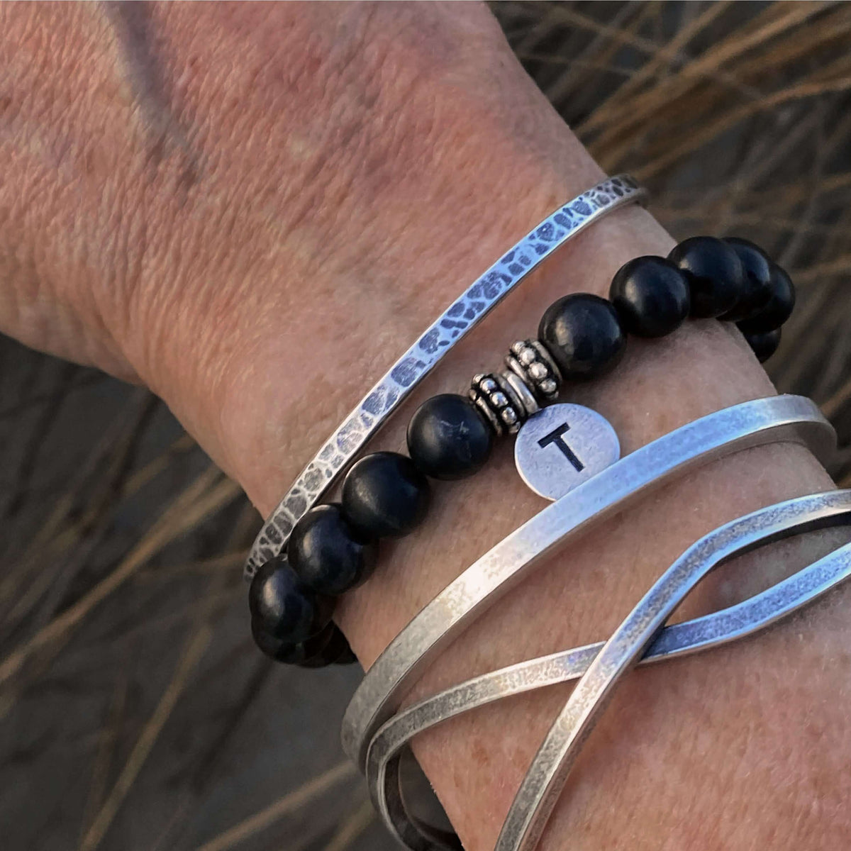 Initial Stretch Bracelet Collection featuring a personalized Shungite bracelet with an initial disk and silver bangles.