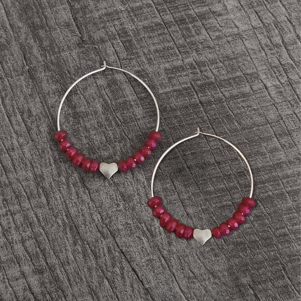 Love Earrings - Beaded hoop earrings with heart and ruby jade on a textured wooden background.