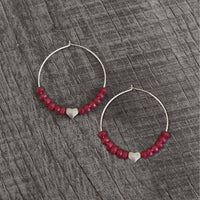 Love Earrings - Beaded hoop earrings with heart and ruby jade on a textured wooden background.