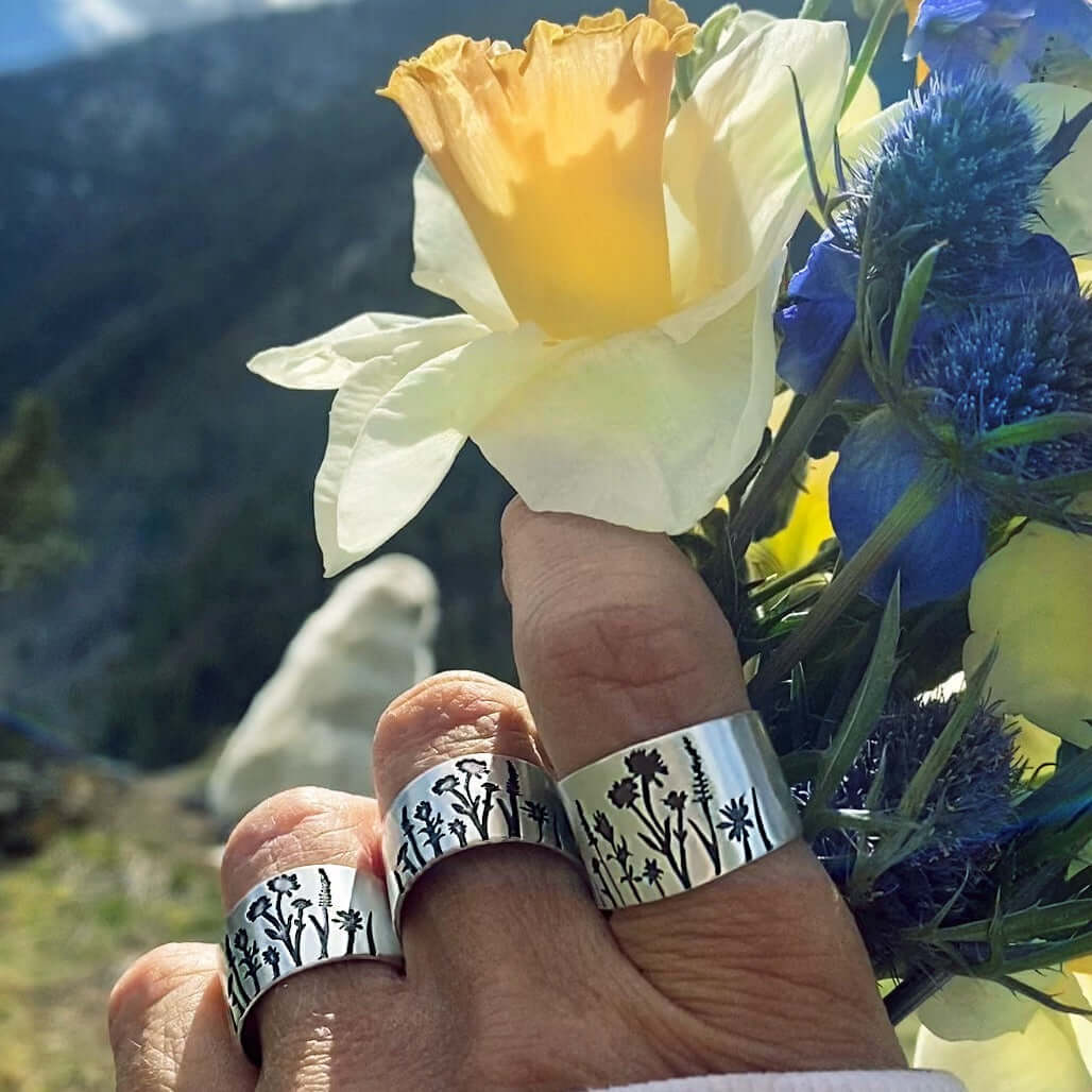 Wildflowers Adjustable Ring displayed on hand with wildflowers and a yellow flower in nature background.
