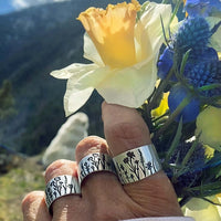 Wildflowers Adjustable Ring displayed on hand with wildflowers and a yellow flower in nature background.