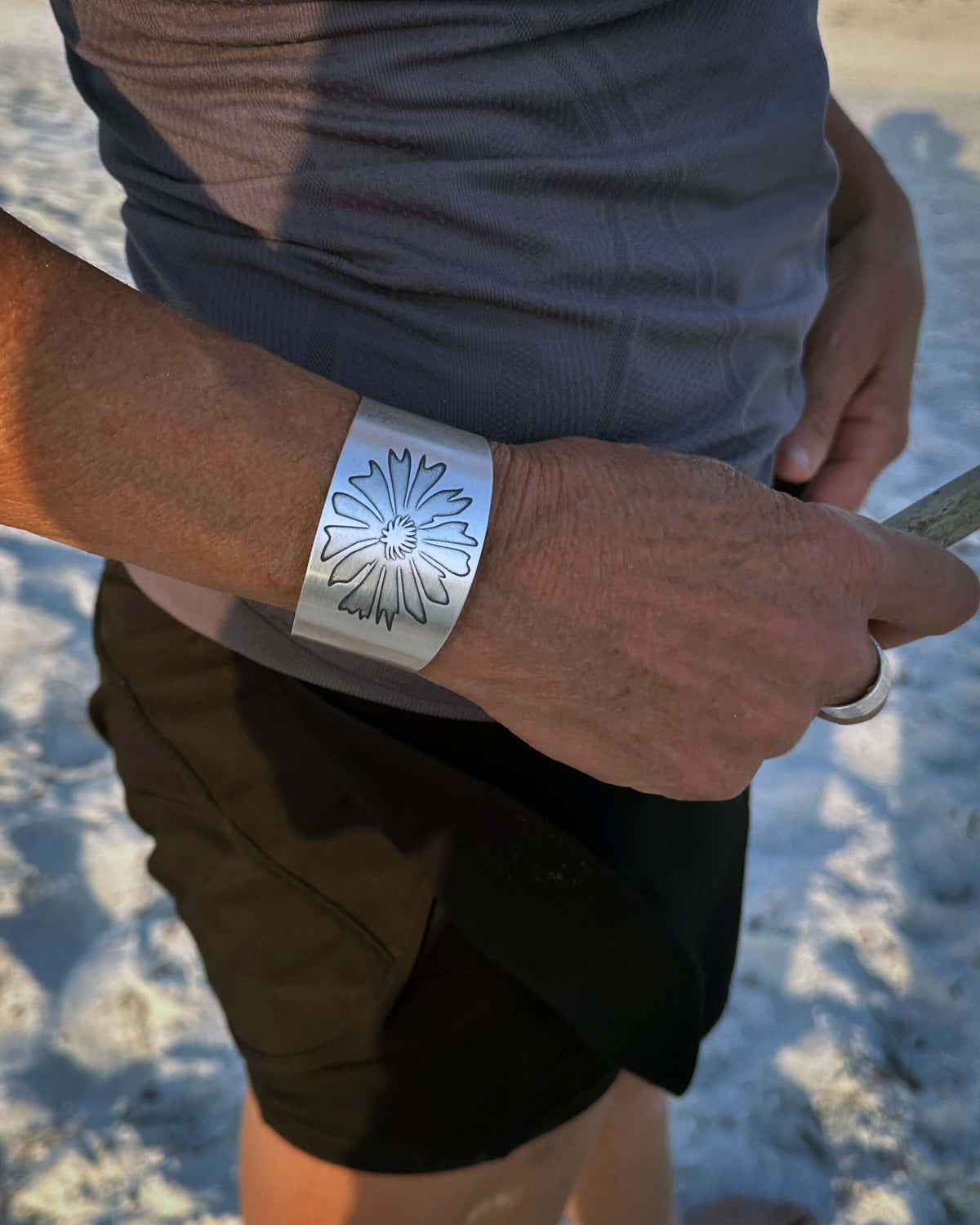 Matte silver Bitterroot flower cuff bracelet worn on a beach, showcasing its floral design and adjustable fit.