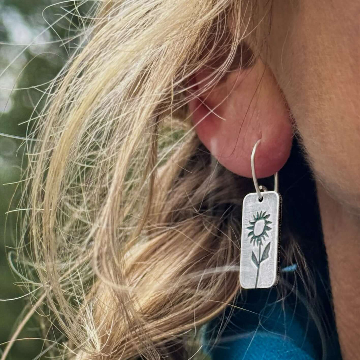 Balsamroot Flower Earrings in matte silver finish worn by a person outdoors with long hair.