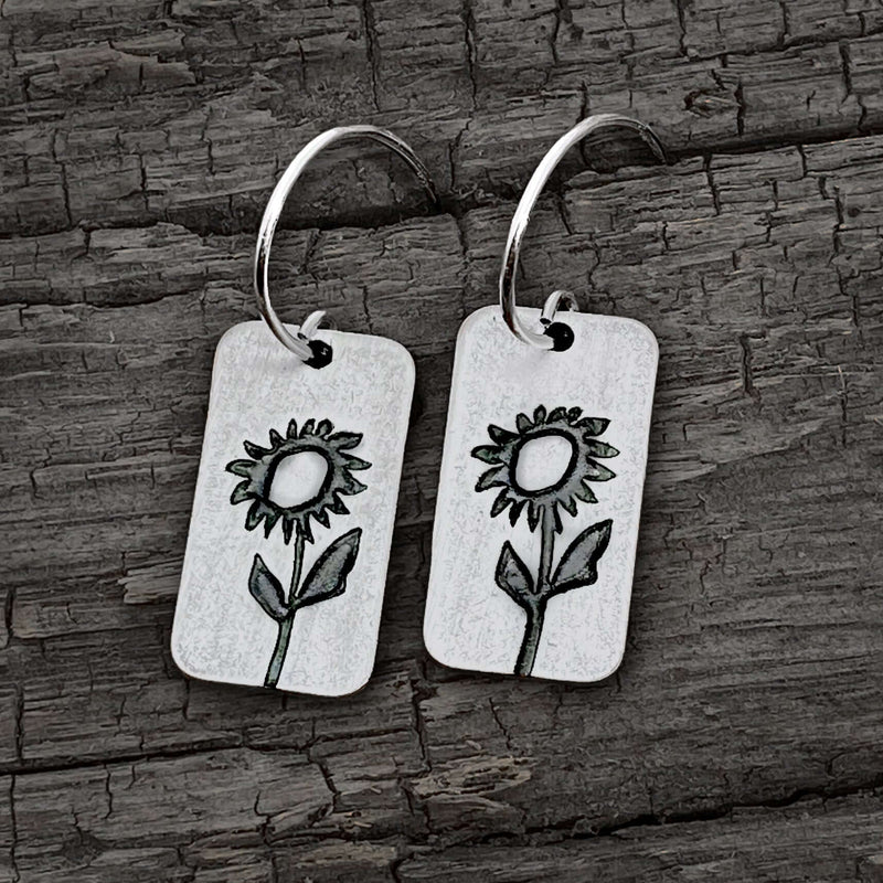 Balsamroot Flower Earrings in matte silver finish featuring floral engravings on a rustic wooden background.