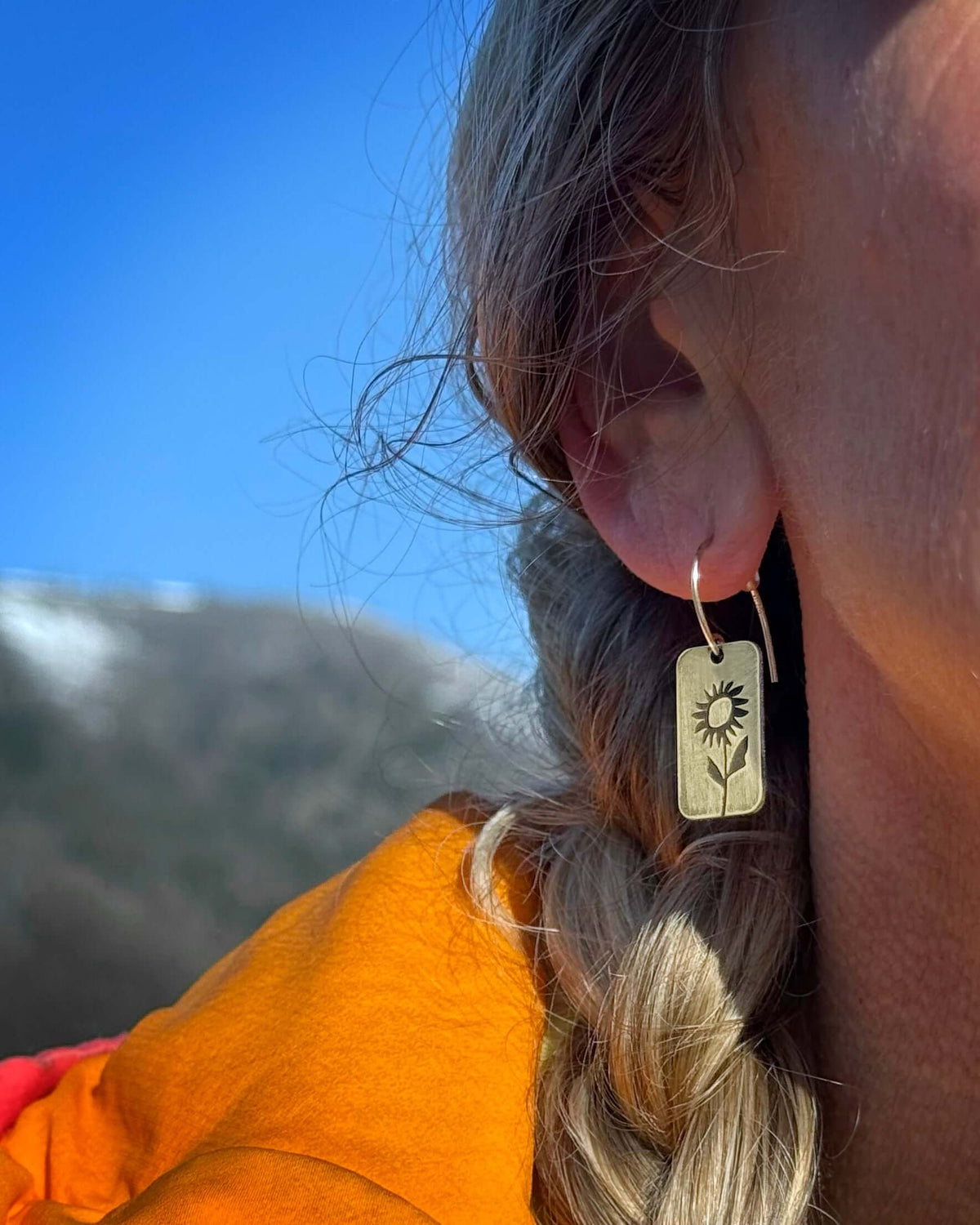 Balsamroot Flower Earrings displayed on a woman outdoors, featuring a design inspired by the Arrowleaf Balsamroot flower.