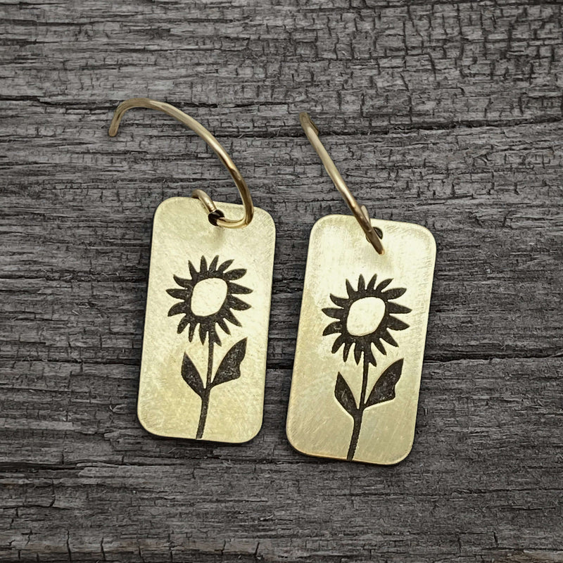 Balsamroot Flower Earrings in antique brass with sunflower design on reclaimed wood background.