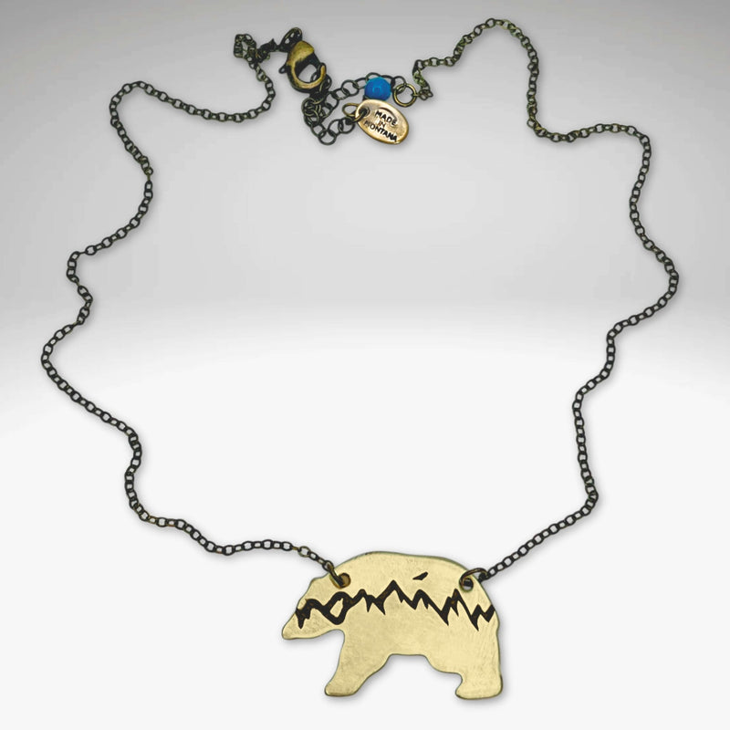 Bears in the Mountains Necklace featuring a bear and mountain design, handmade in matte brass on an 18" cable chain.