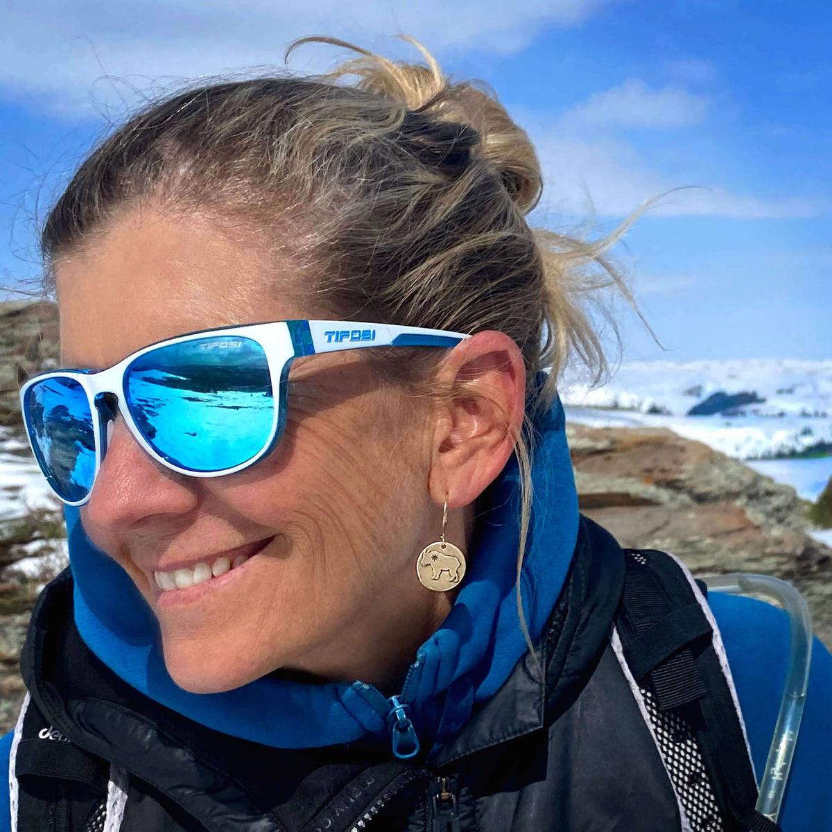 Woman wearing Billy Goat Earrings and sunglasses outdoors, showcasing a unique style with a winter backdrop.