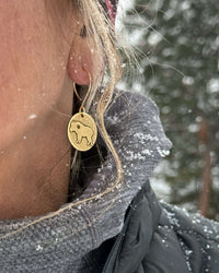 Billy Goat Earrings worn by a woman with snowfall in the background, featuring a tiny star inside the goat design.