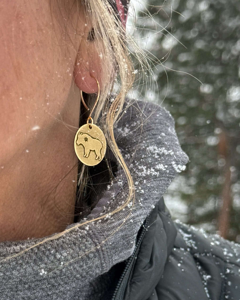 Billy Goat Earrings worn by a woman with snowfall in the background, featuring a tiny star inside the goat design.