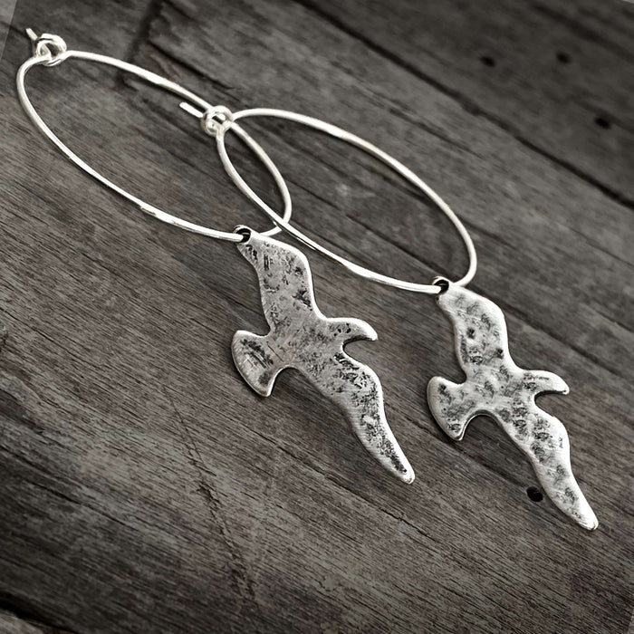 Birds on a Wire Hoop Earrings featuring hammered birds and silver hoops on a rustic wooden background.