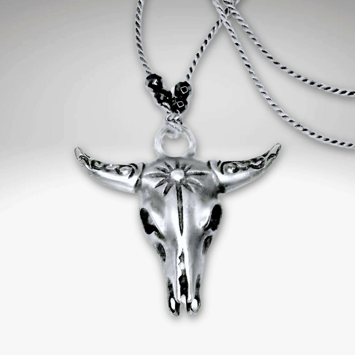 Bison Skull Necklace in matte silver finish with intricate detailing, hanging on a silk cord with hematite beads.