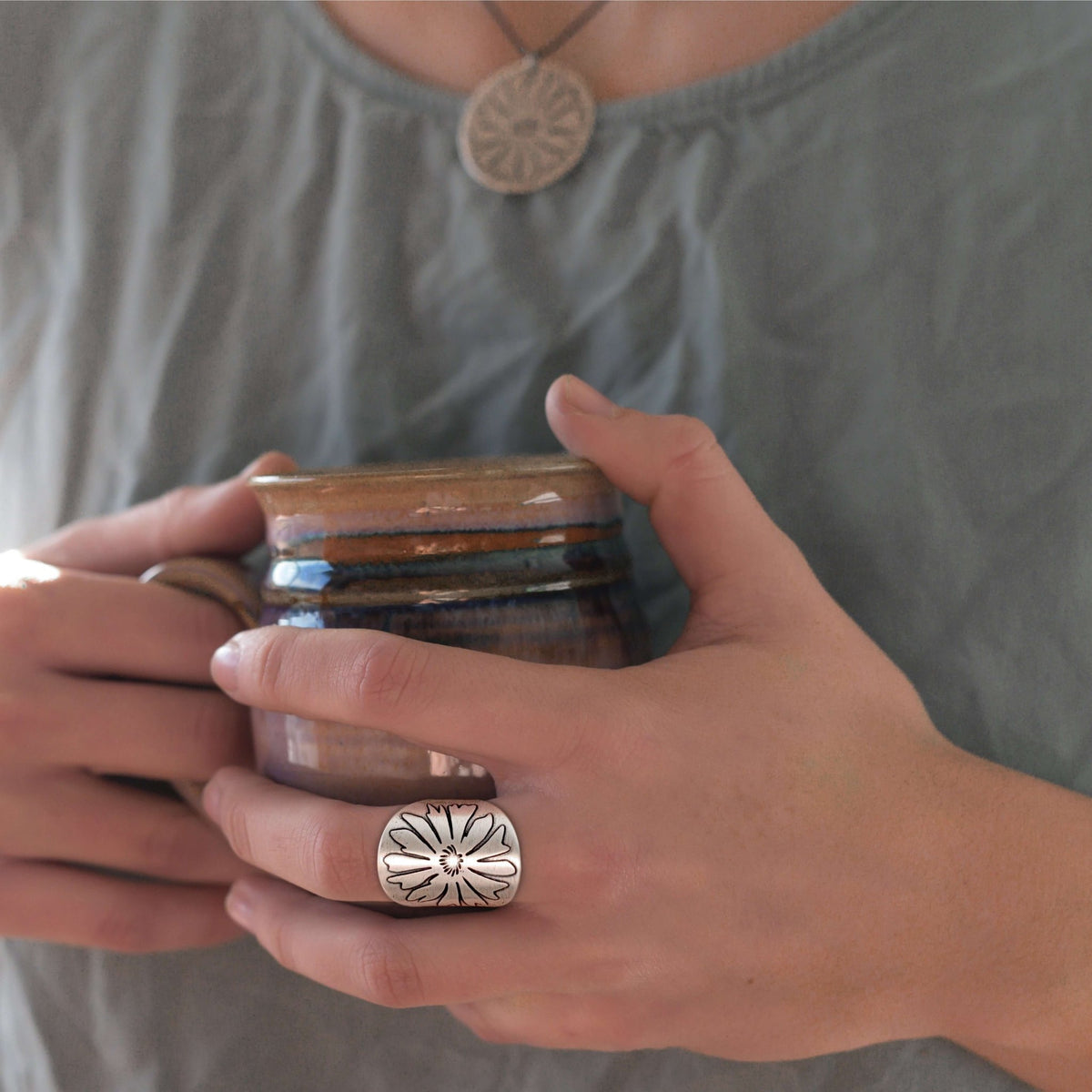 Person holding a mug and wearing the Bitterroot Wildflower Adjustable Ring in matte silver.
