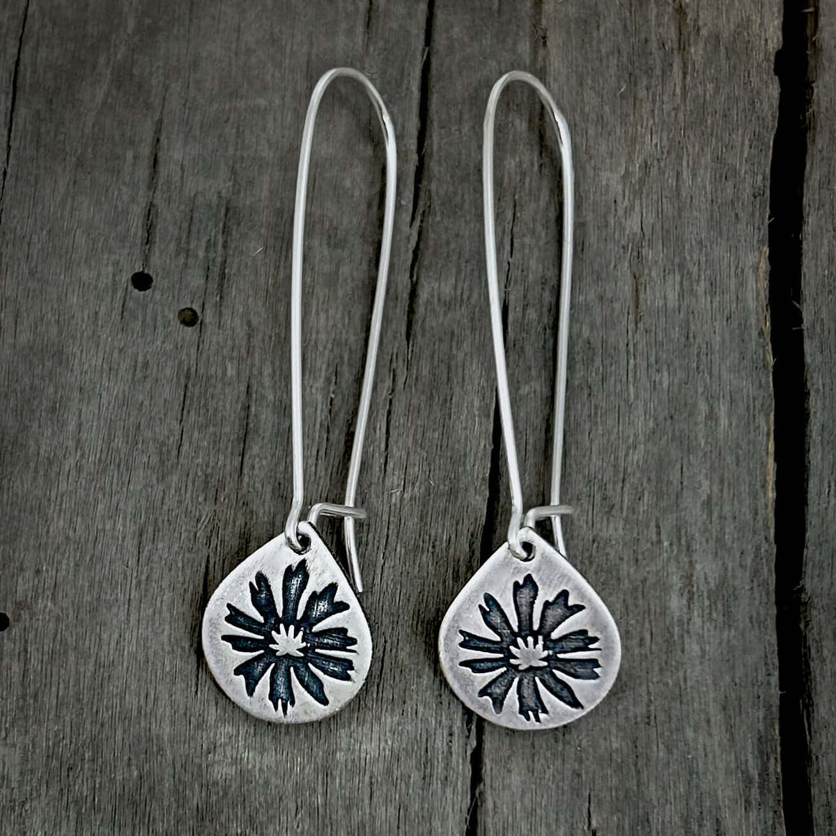 Bitterroot Drop Earrings in matte silver with kidney earwire on wooden background.
