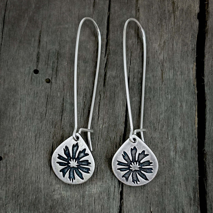 Bitterroot Drop Earrings in matte silver with kidney earwire on wooden background.