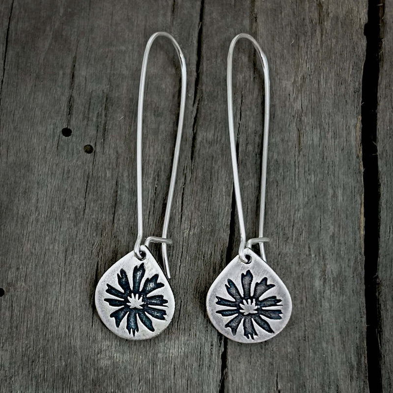 Bitterroot Drop Earrings in matte silver with kidney earwire on wooden background.