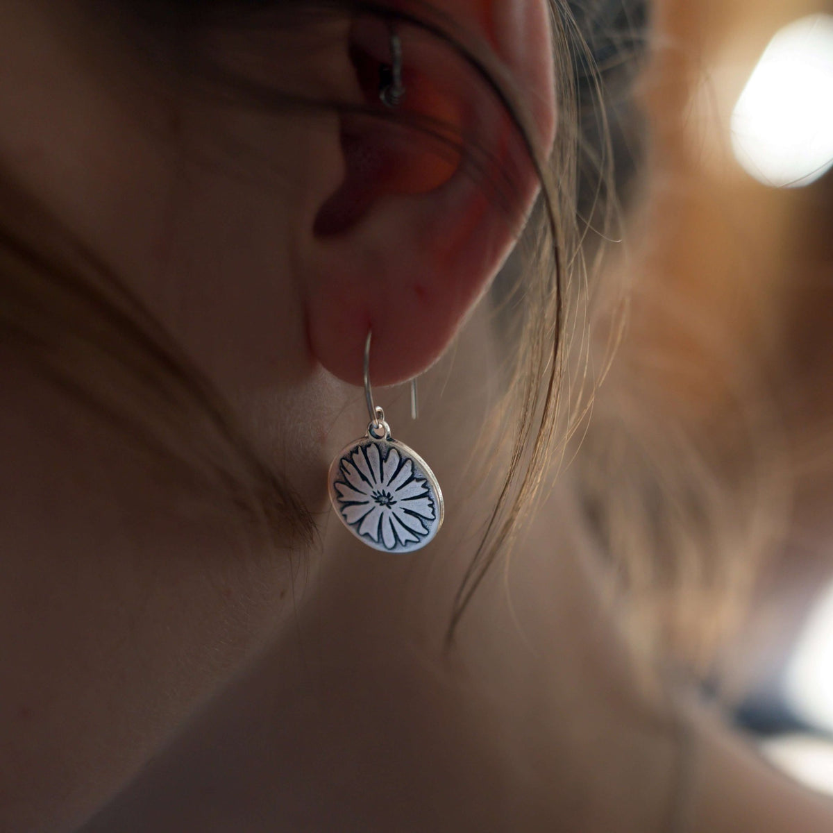 Bitterroot Flower Earrings showcased on a model's ear, featuring intricate flower design in a stunning silver finish.