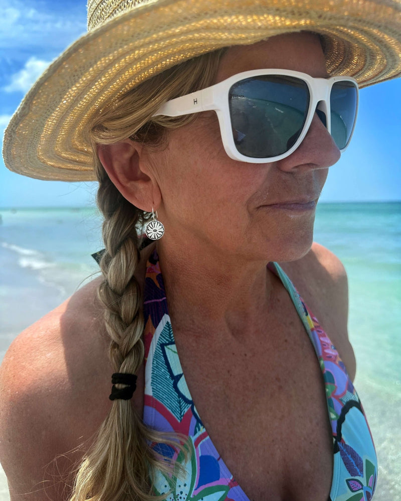 Bitterroot Flower Earrings worn by a woman with sunglasses on a beach, highlighting their beauty and style.