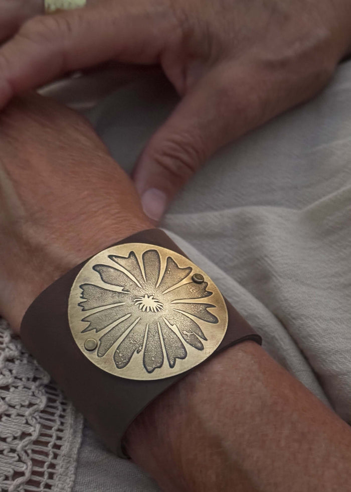 Bitterroot Leather Cuff on a wrist featuring a floral design in antique brass finish.