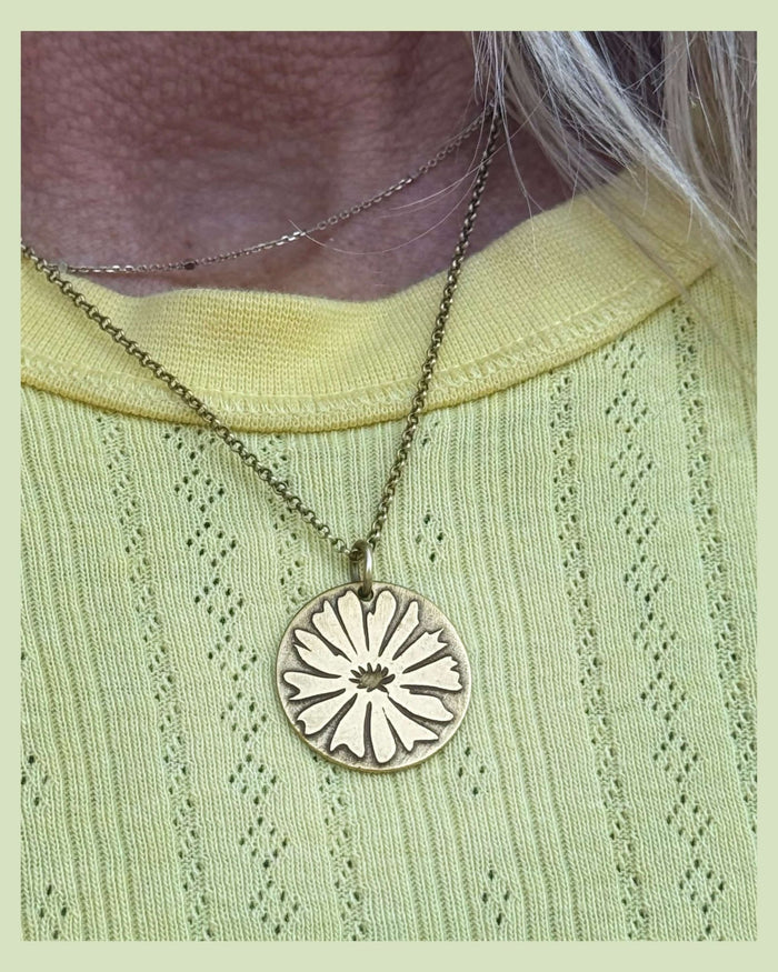 Antique brass Bitterroot pendant on a gold plated chain on a woman with a yellow sweater.