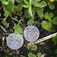 Blossom Earrings resting among greenery, featuring modern floral design in silver finish.