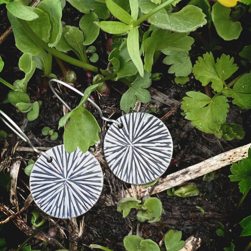 Blossom Earrings resting among greenery, featuring modern floral design in silver finish.