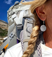 Woman wearing Blossom Earrings while hiking with a backpack in a scenic outdoor setting.