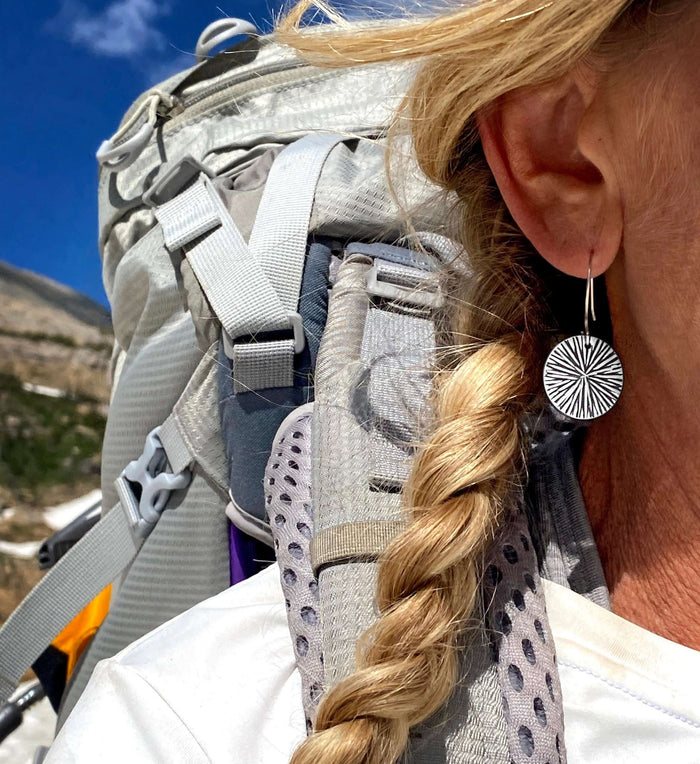 Woman wearing Blossom Earrings while hiking with a backpack in a scenic outdoor setting.