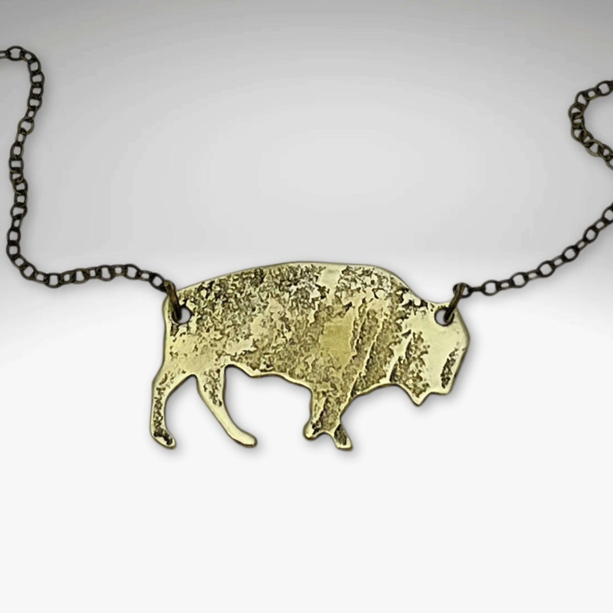 Buffalo Necklace features a rustic buffalo pendant in antique brass on a chain, adjustable to 30 inches.