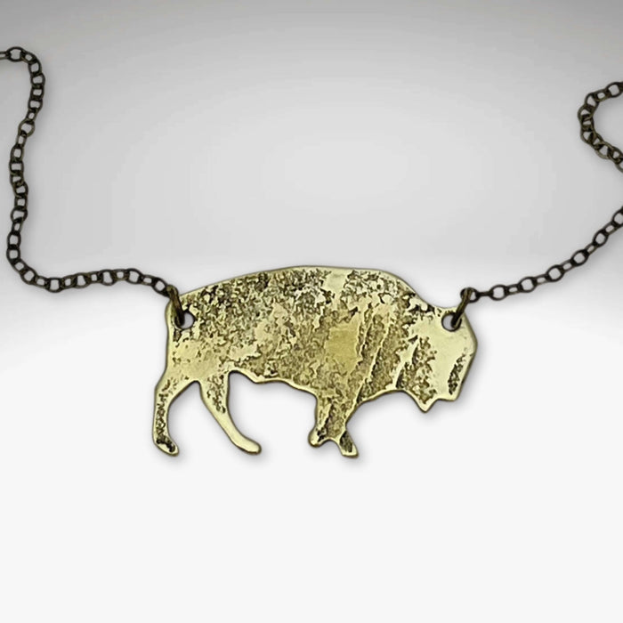 Buffalo Necklace features a rustic buffalo pendant in antique brass on a chain, adjustable to 30 inches.
