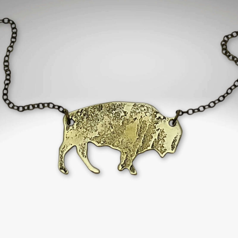 Buffalo Necklace features a rustic buffalo pendant in antique brass on a chain, adjustable to 30 inches.