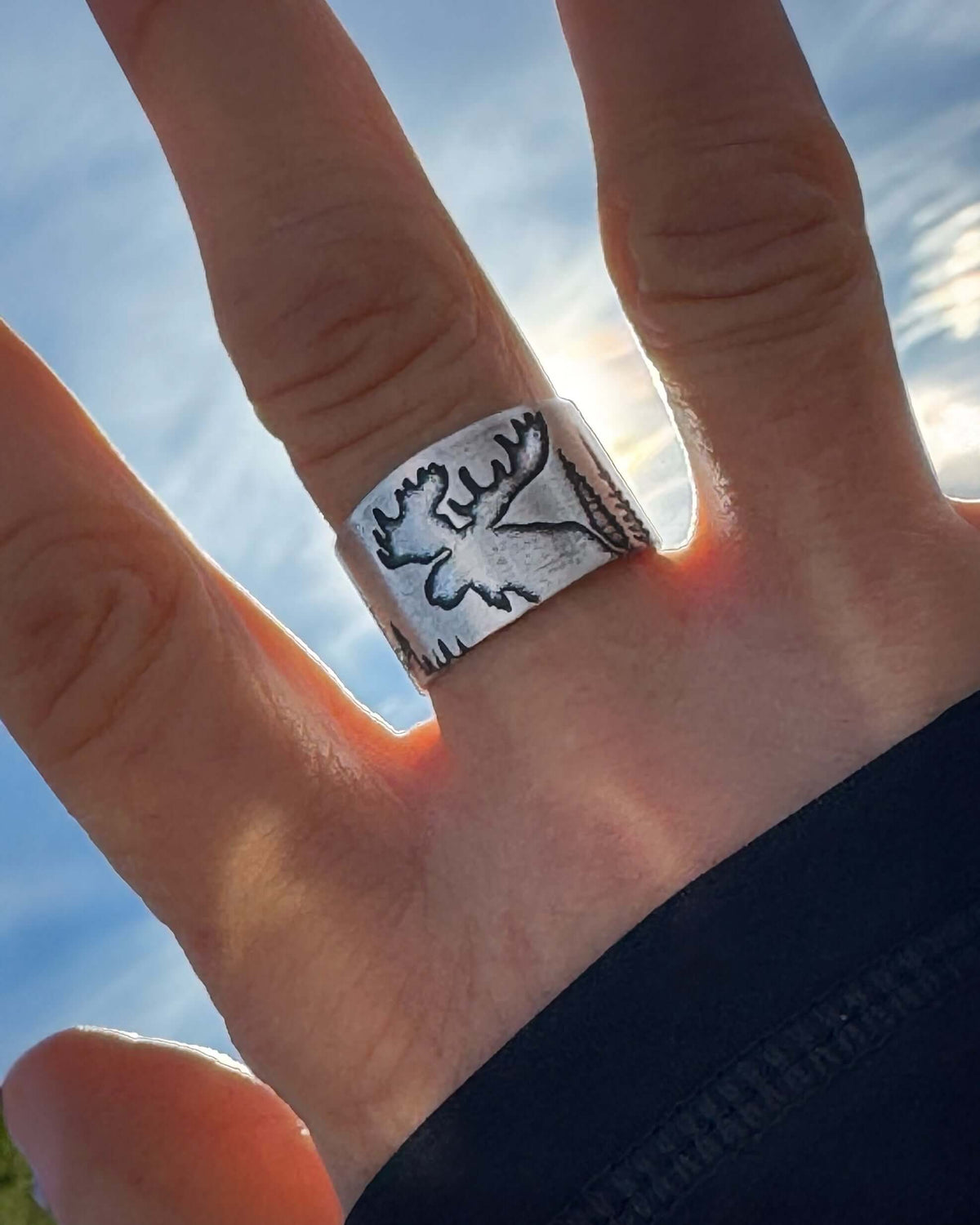 Creek Moose Adjustable Ring worn on a hand with a scenic sky backdrop.