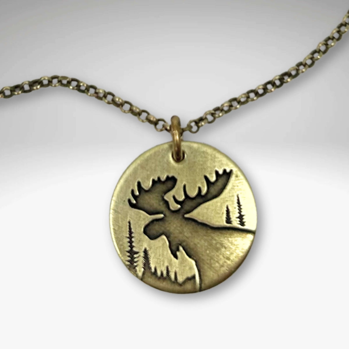 Creek Moose Necklace pendant on antique brass chain with moose and tree design, handmade in Montana.