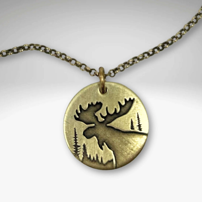 Creek Moose Necklace pendant on antique brass chain with moose and tree design, handmade in Montana.