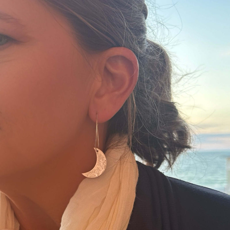 Crescent Moon Hoop Earrings worn by a woman, featuring a hammered brass texture and a serene background.