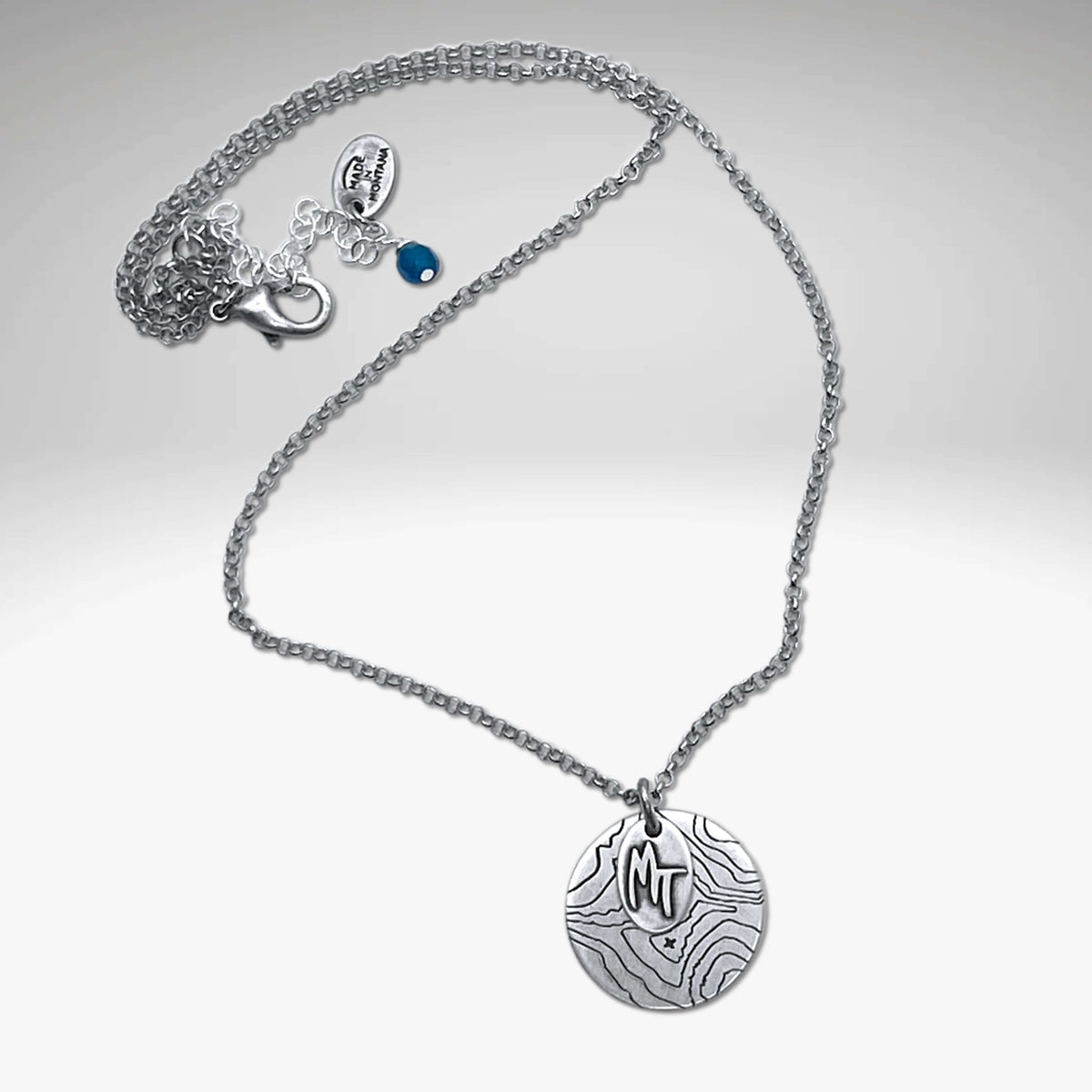 Explore MT Necklace featuring a topographic map design and MT etched on a round disk in Matte Silver.