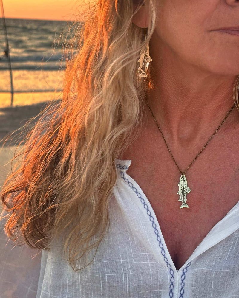Daphne Lorna Fishing Trout Earrings – Handmade Montana Wildlife Jewelry, Matte Silver or Antique Brass worn by a woman at sunset.