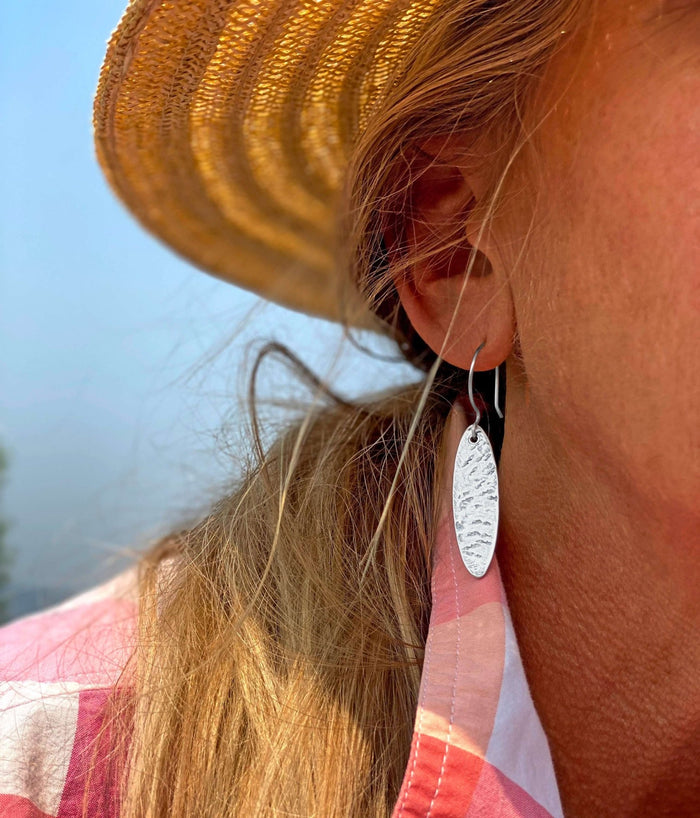 Fog Drop Earrings worn by a woman, showcasing the textured design in matte silver against her summer attire.