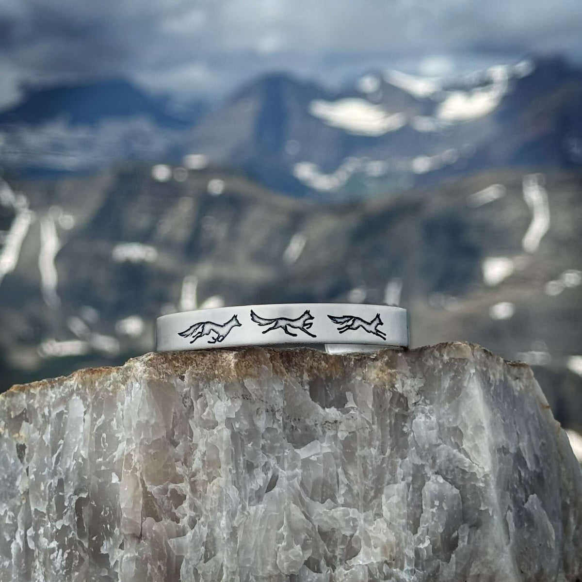 Fox Run Cuff Bracelet featuring playful fox designs, set against a stunning mountain backdrop.