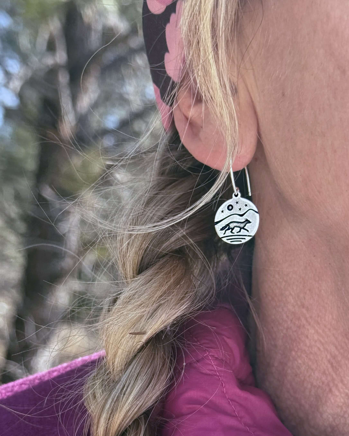 Close-up of a woman wearing Fox Run Earrings, showcasing a fox and mountain design in raw brass with a silver finish.