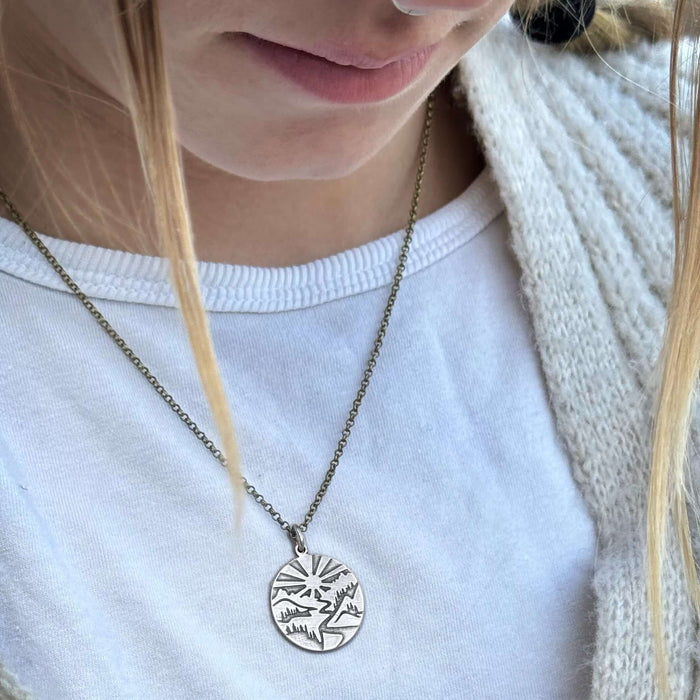 Going to the Sun Necklace featuring a detailed mountain pendant worn by a person, with a lightweight adjustable chain.