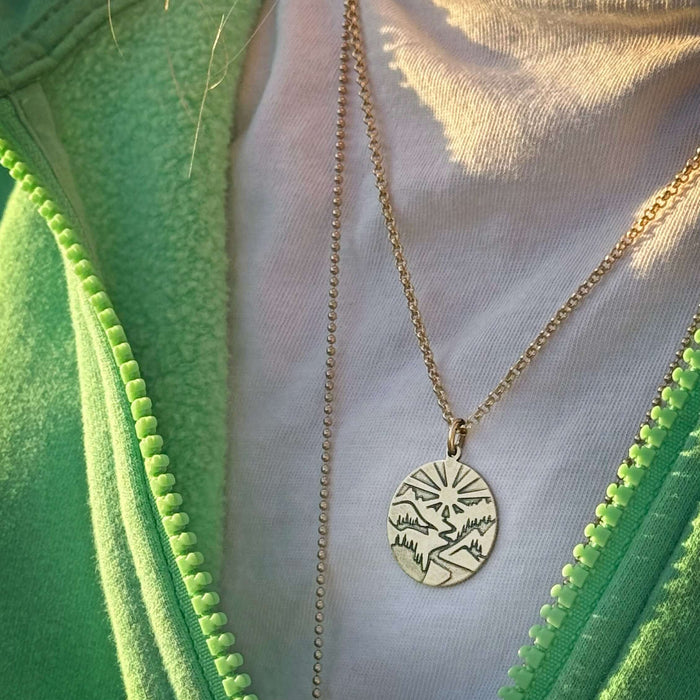 Going to the Sun Necklace worn on a model, featuring a detailed mountain pendant.