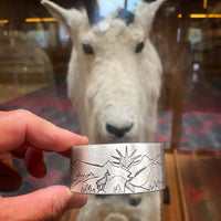 Going to the Sun Road Cuff Bracelet featuring mountains, a sun goat, and road design in front of a mountain goat display.