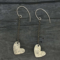 Heart Drop Earrings with hand-hammered asymmetrical hearts and sterling silver earwires on a dark wooden background.