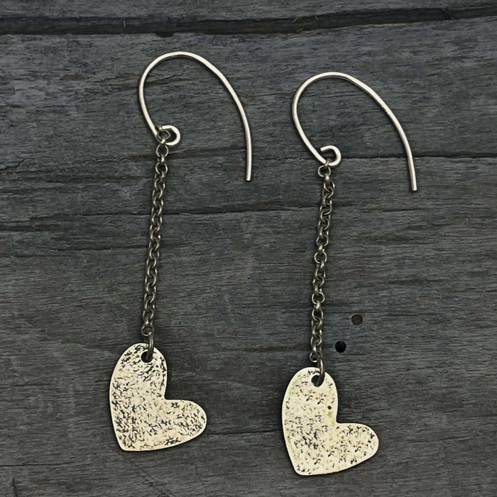 Heart Drop Earrings with hand-hammered asymmetrical hearts and sterling silver earwires on a dark wooden background.