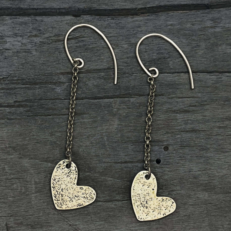 Heart Drop Earrings with hand-hammered asymmetrical hearts and sterling silver earwires on a dark wooden background.