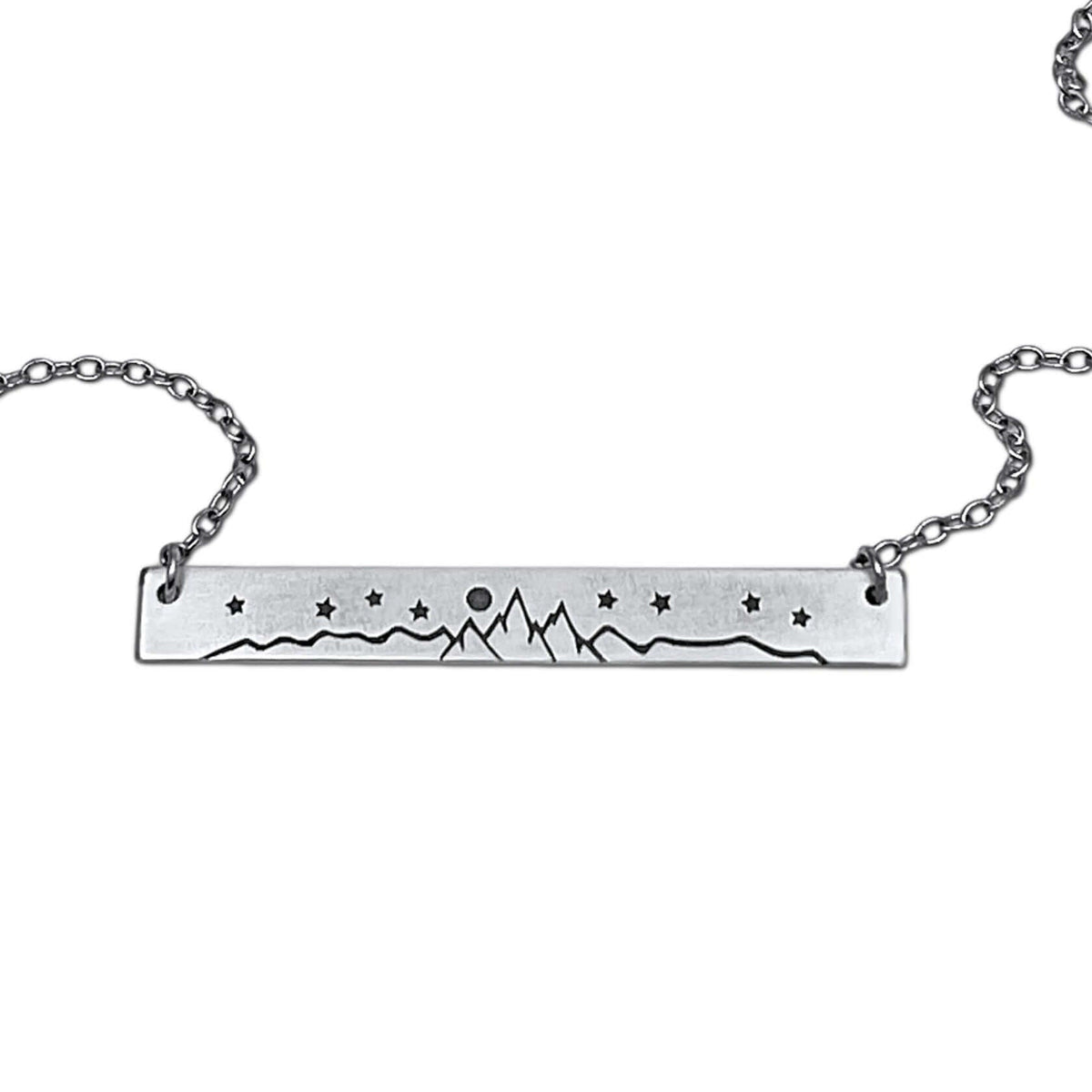 High Alpine Necklace featuring a brass mountain landscape design, adjustable chain, and available in matte silver and antique brass finishes.